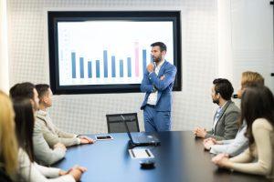 Man standing infront of audio visual screen with staff